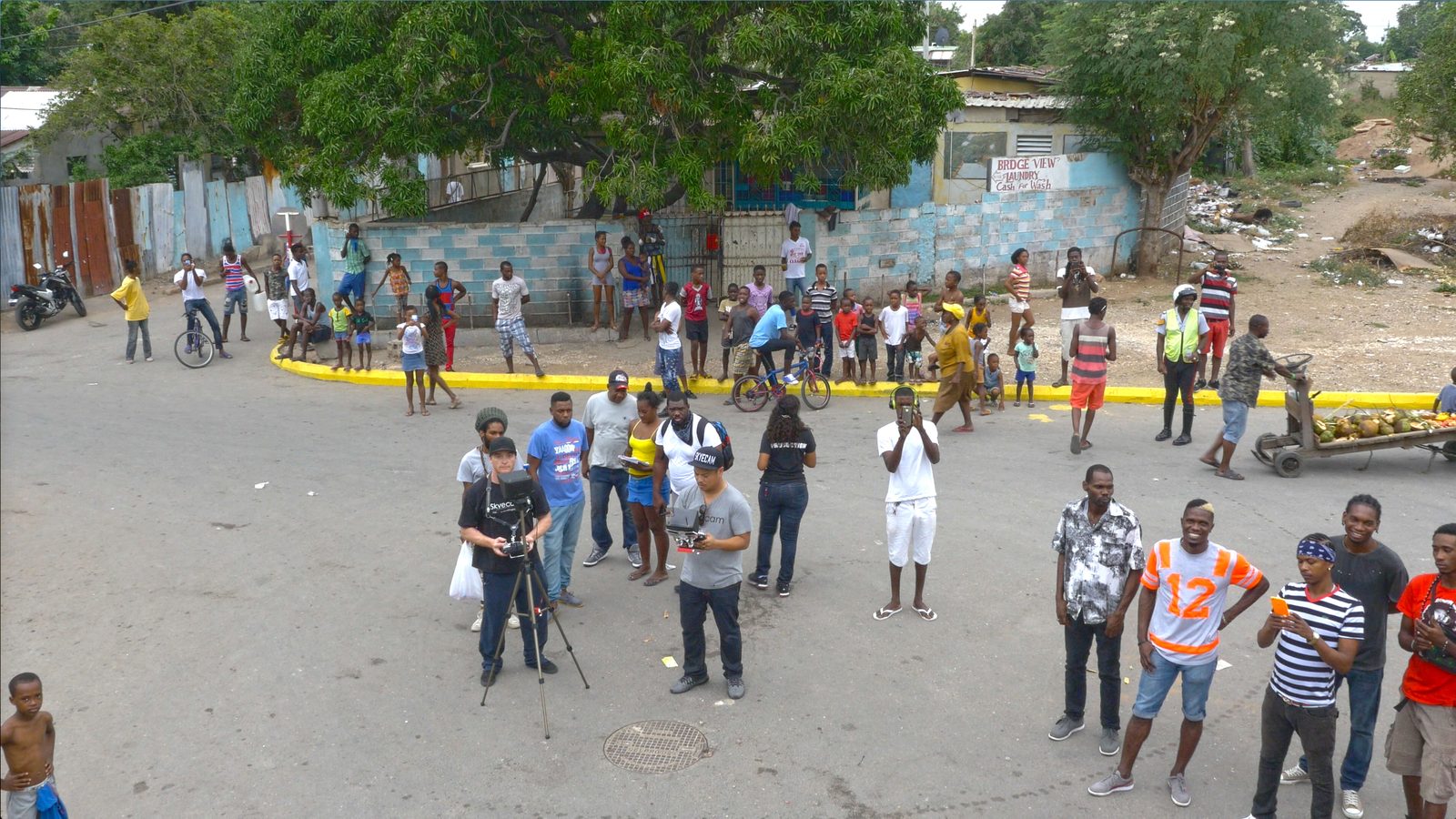 On a street, film crew with camera, onlookers behind a tape line