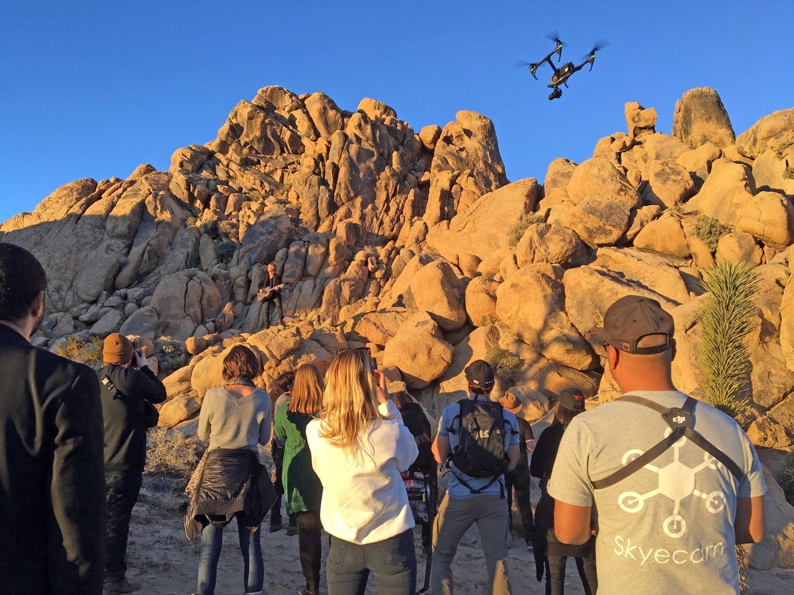 A crew watches an aircraft fly over a formation of large boulders