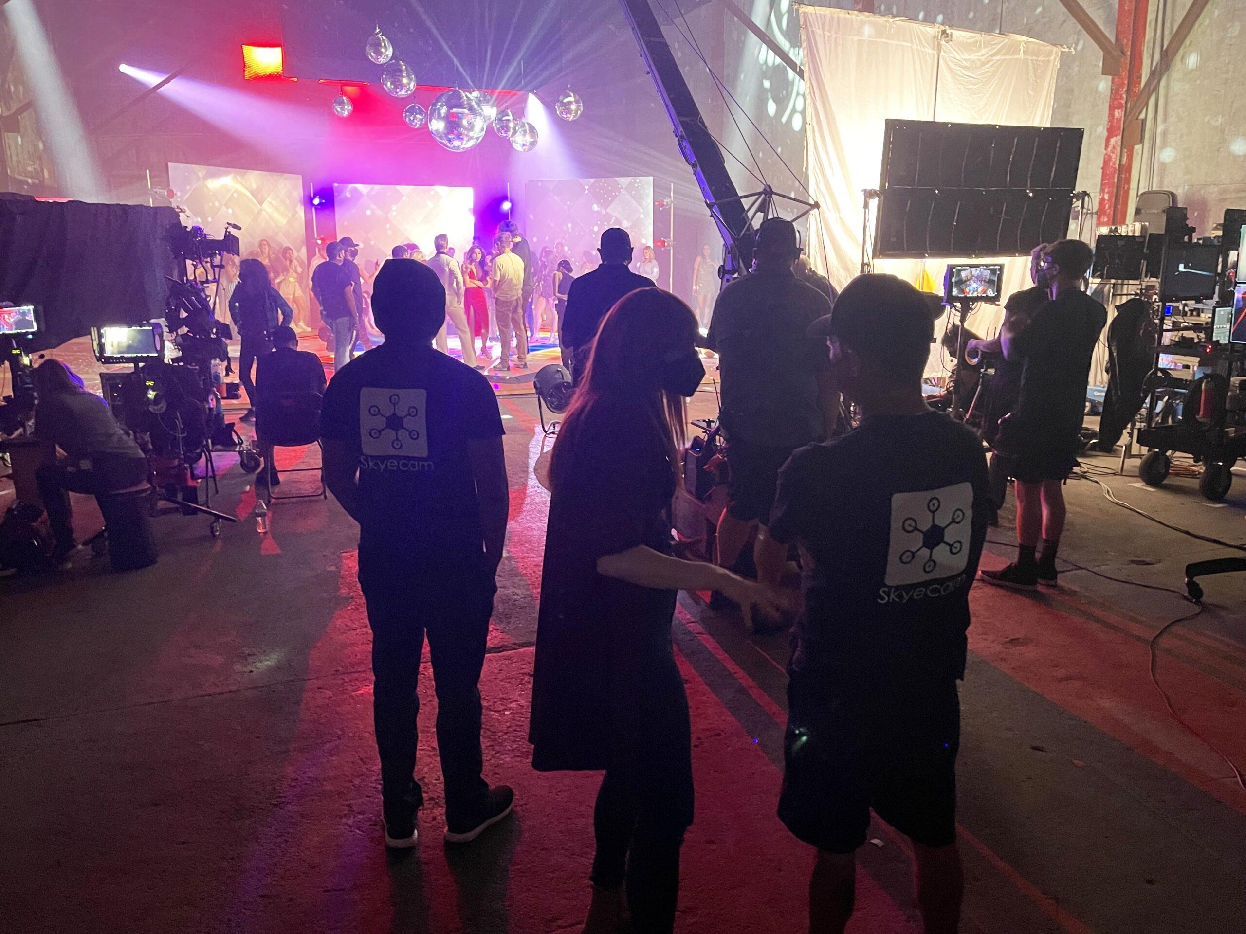 From behind the camera, crew in Skyecam shirts watch a lit stage set