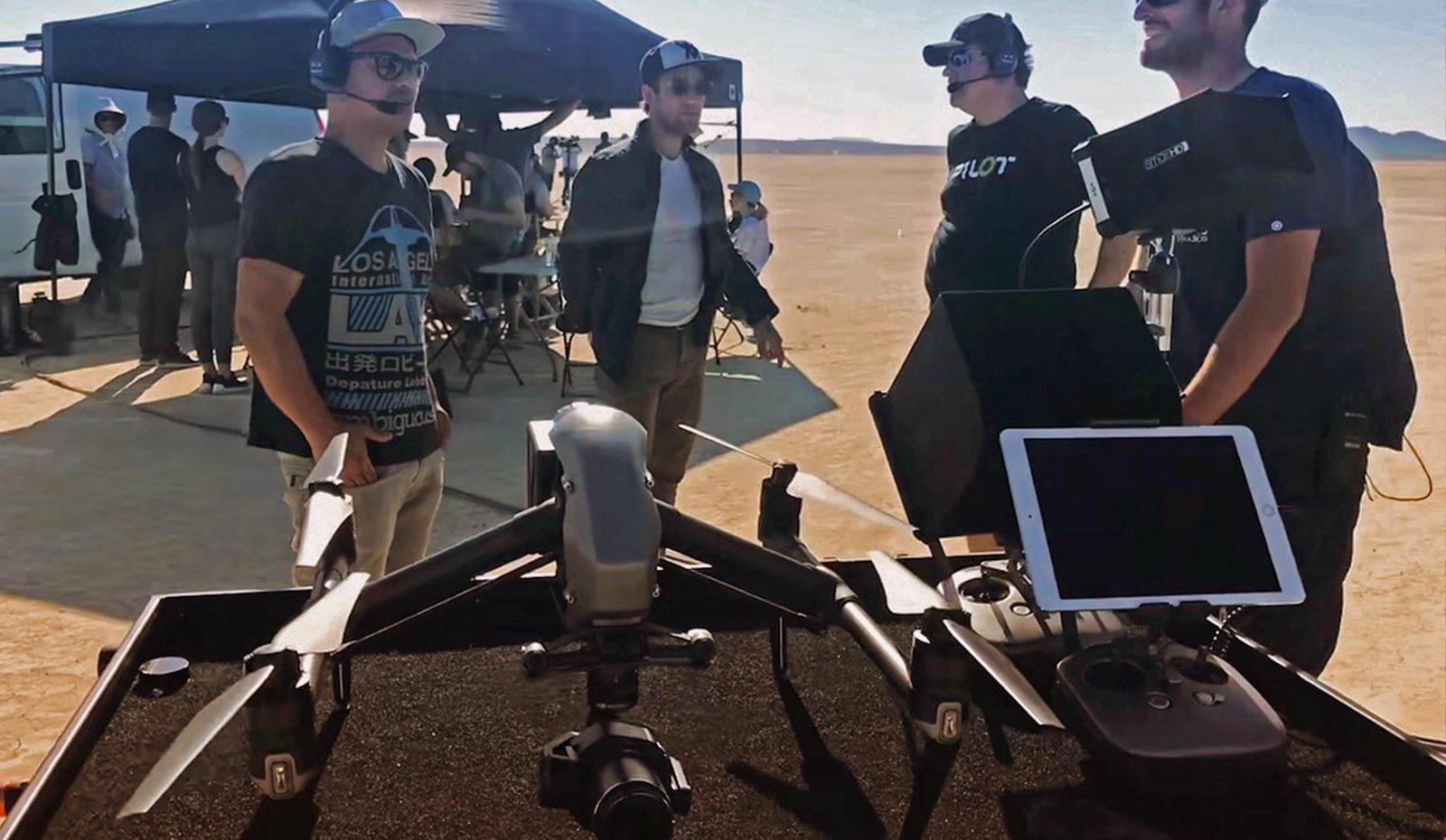 Crew gathered around a drone and monitor under a pop-up tent on desert shoot